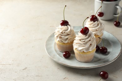 Delicious cupcakes with cream and cherries on light textured table, space for text