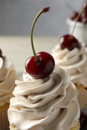 Delicious cupcakes with cream and cherries on table, closeup