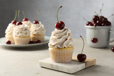 Delicious cupcakes with cream and cherries on light textured table