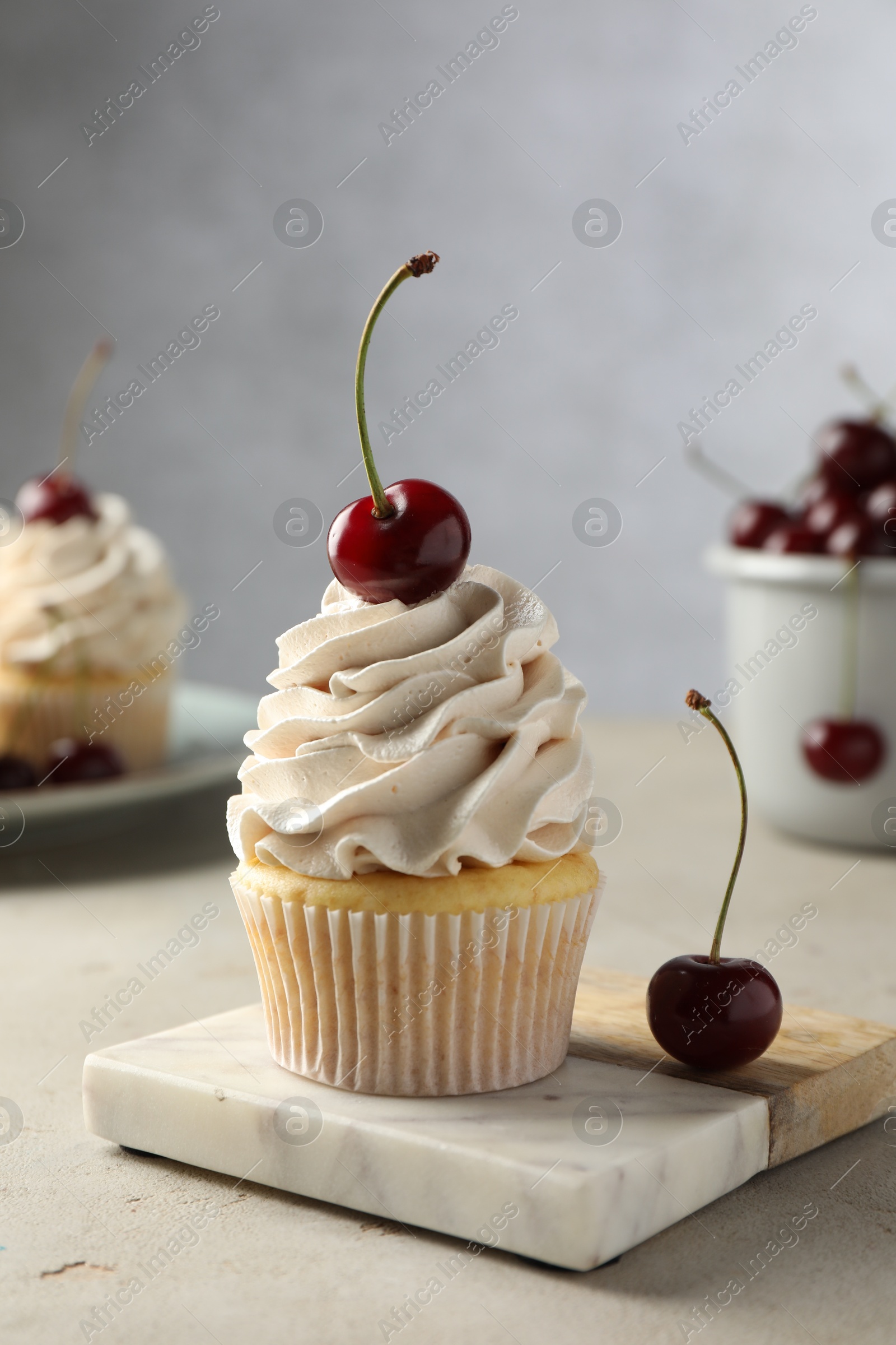 Photo of Delicious cupcake with cream and cherries on light textured table