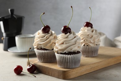 Photo of Delicious cupcakes with cream and cherries on light textured table, closeup