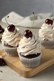 Delicious cupcakes with cream and cherries on light textured table, closeup