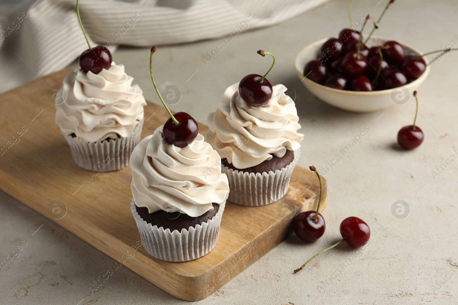 Photo of Delicious cupcakes with cream and cherries on light textured table