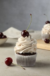 Photo of Delicious cupcake with cream and cherries on light textured table