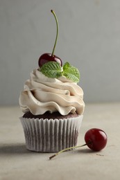 Delicious cupcake with cherries and fresh mint on light textured table, closeup