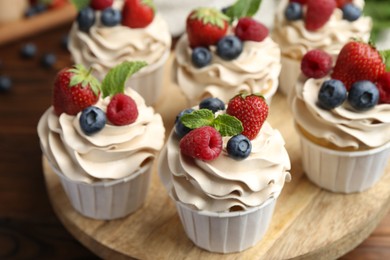 Photo of Tasty cupcakes with different berries and mint on wooden table, closeup