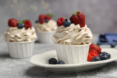 Photo of Tasty cupcakes with different berries on light grey table, closeup