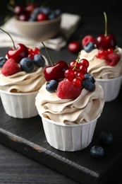 Photo of Tasty cupcakes with different berries on black wooden table, closeup