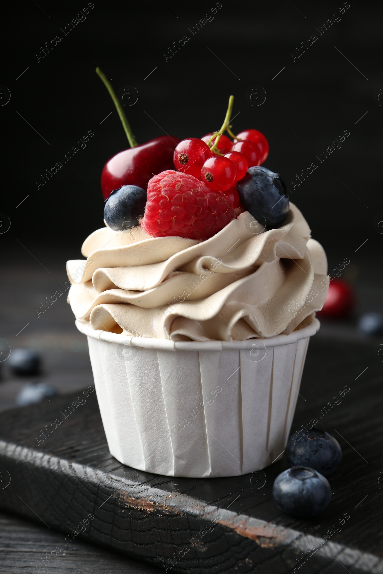 Photo of Tasty cupcake with different berries on black wooden table, closeup