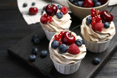 Photo of Tasty cupcakes with different berries on black wooden table, closeup