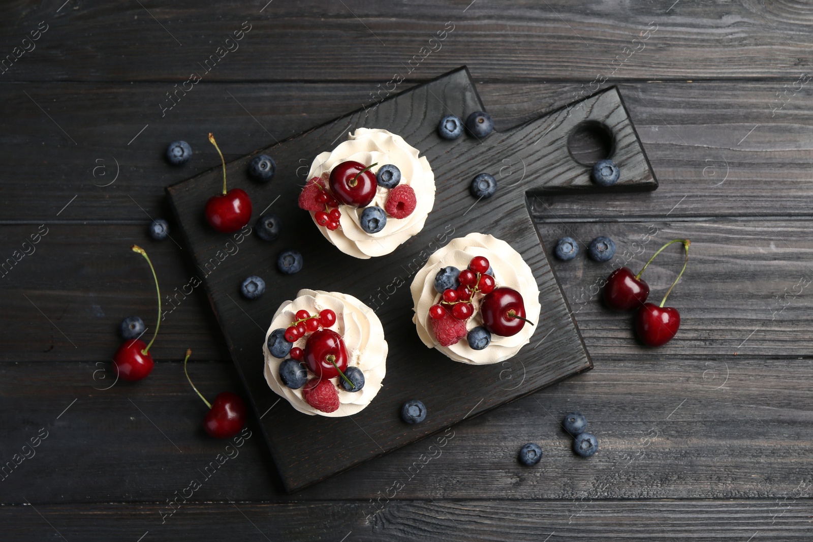 Photo of Tasty cupcakes with different berries on black wooden table, flat lay