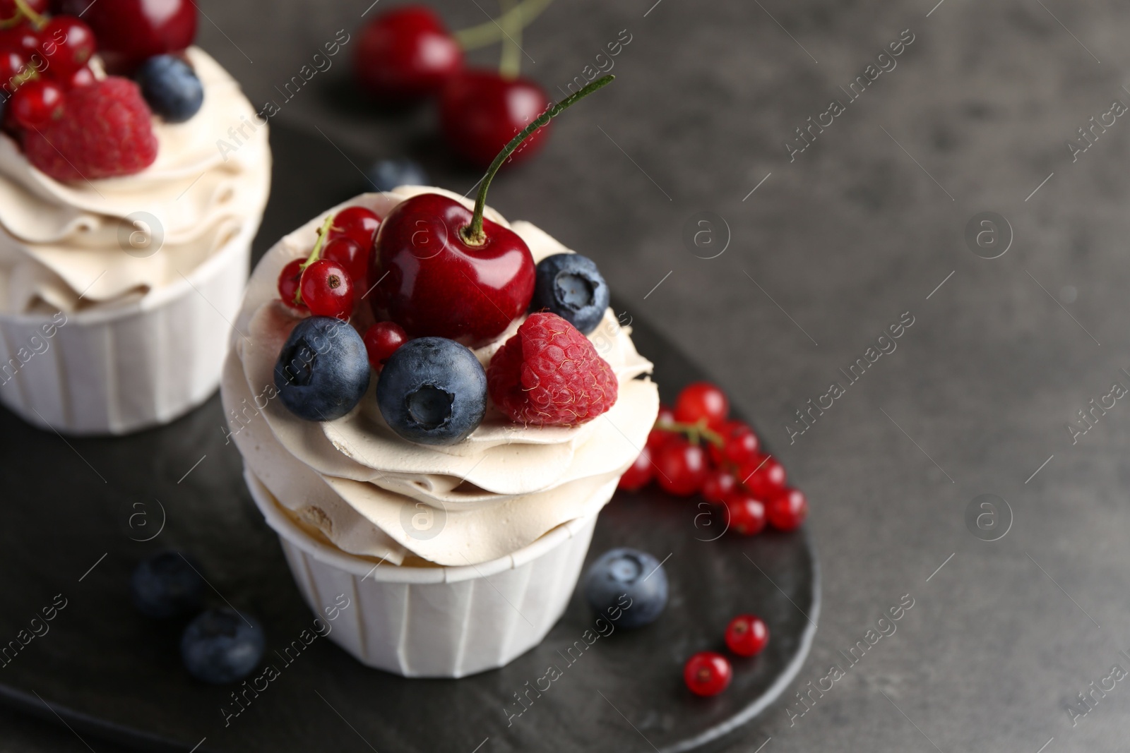 Photo of Tasty cupcakes with different berries on grey table, closeup. Space for text