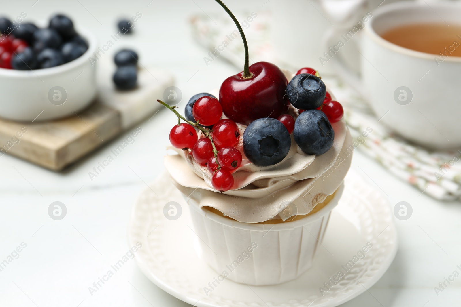 Photo of Tasty cupcake with different berries and tea on white marble table, closeup