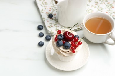 Tasty cupcake with different berries and tea on white marble table, space for text