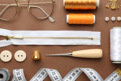 Flat lay composition with different sewing supplies and glasses on brown background