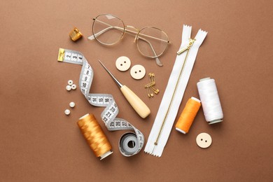 Photo of Flat lay composition with different sewing supplies and glasses on brown background