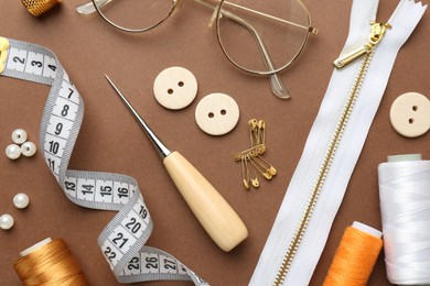 Photo of Flat lay composition with different sewing supplies and glasses on brown background