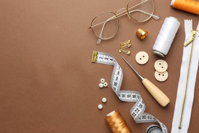 Photo of Flat lay composition with different sewing supplies and glasses on brown background. Space for text