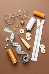 Photo of Flat lay composition with different sewing supplies and glasses on brown background