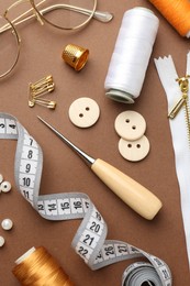 Photo of Flat lay composition with different sewing supplies and glasses on brown background