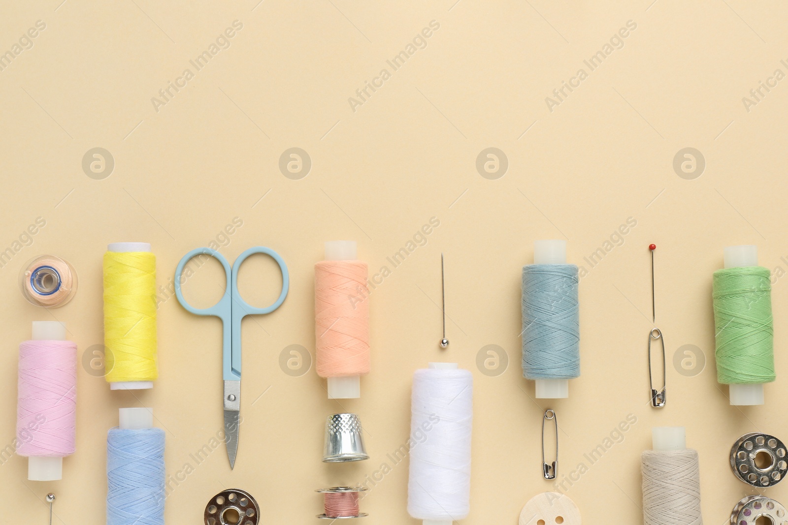 Photo of Flat lay composition with different sewing supplies on beige background. Space for text