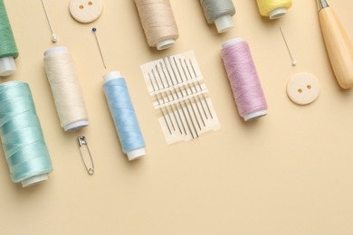 Photo of Flat lay composition with different sewing supplies on beige background. Space for text