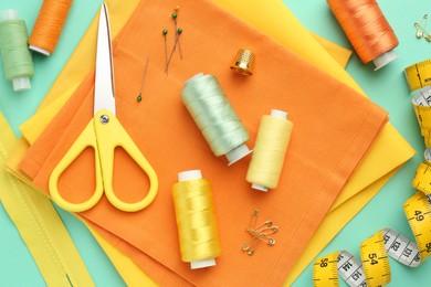 Flat lay composition with different sewing supplies on turquoise background