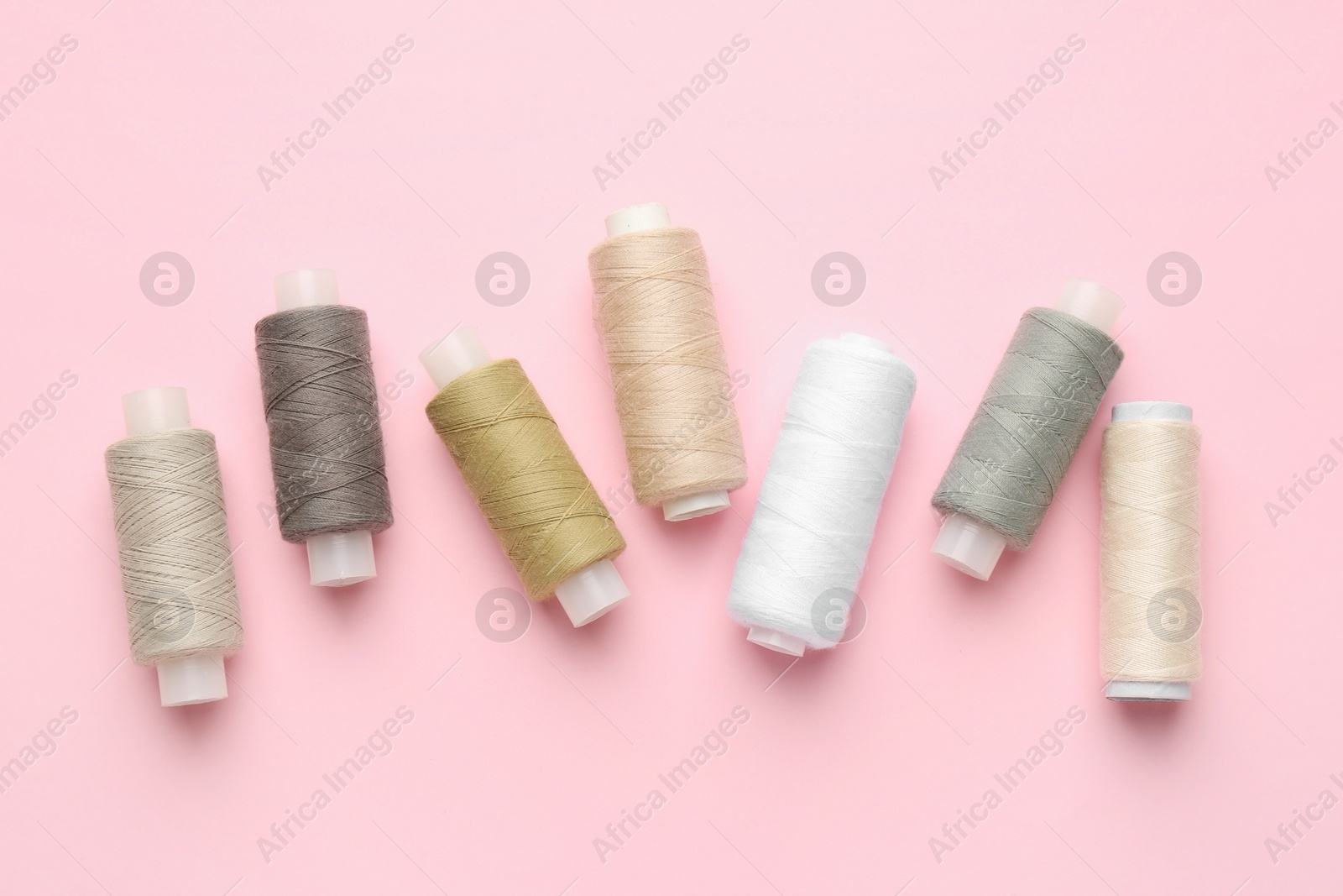 Photo of Flat lay composition with spools of sewing threads on pink background