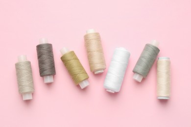 Flat lay composition with spools of sewing threads on pink background