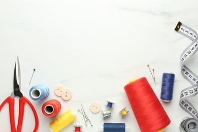 Flat lay composition with different sewing supplies on white marble table. Space for text