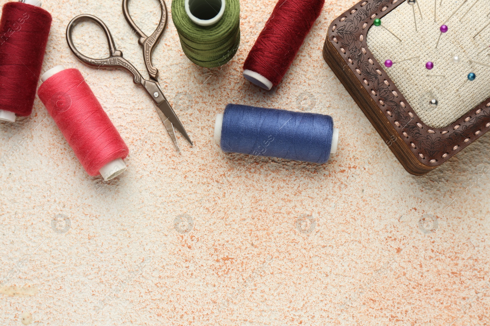 Photo of Flat lay composition with different sewing supplies on beige textured table. Space for text