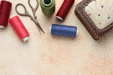 Flat lay composition with different sewing supplies on beige textured table. Space for text