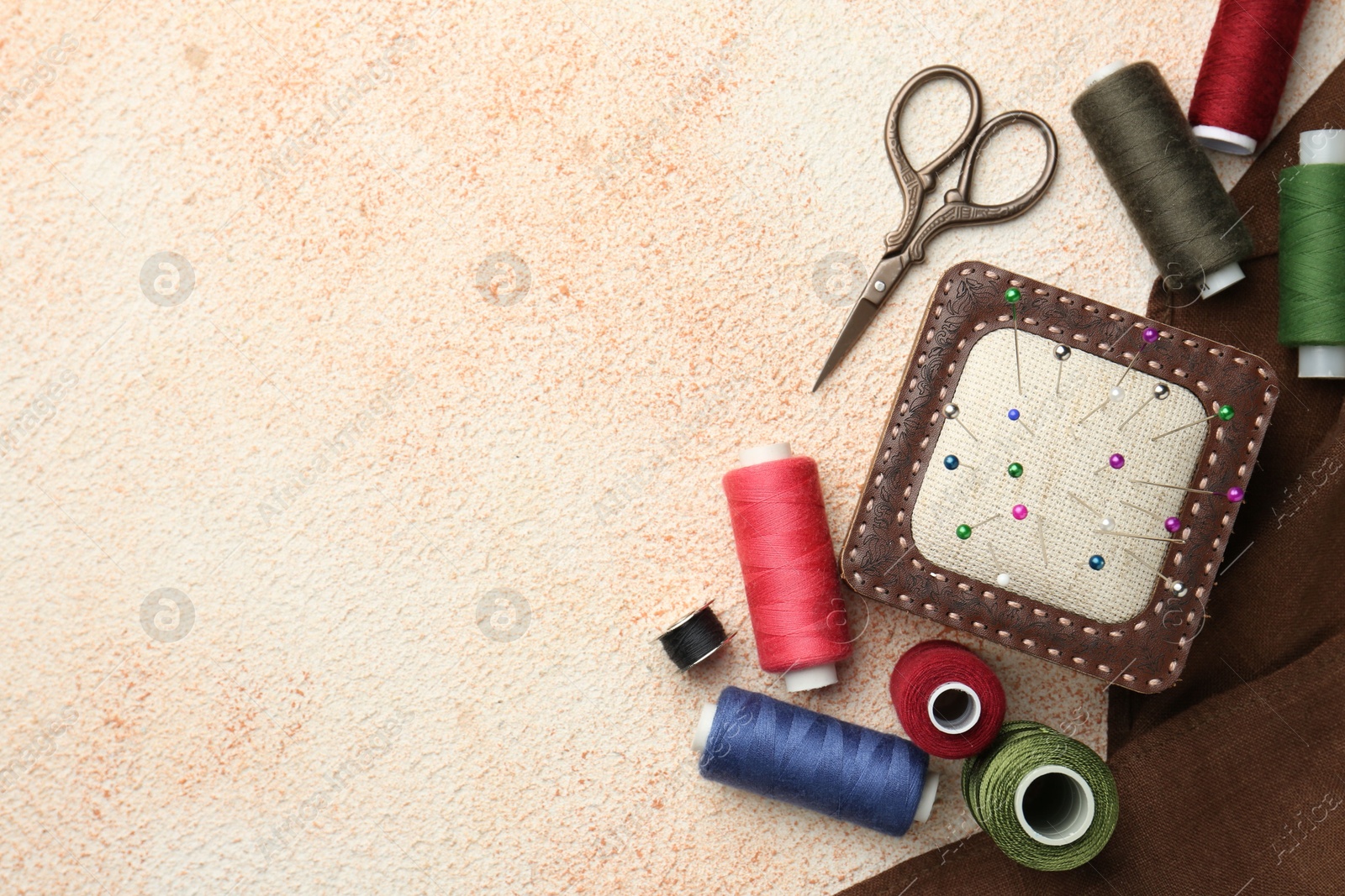 Photo of Flat lay composition with different sewing supplies on beige textured table. Space for text