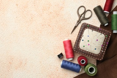 Photo of Flat lay composition with different sewing supplies on beige textured table. Space for text