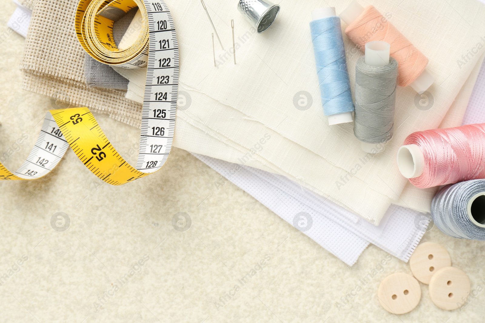 Photo of Flat lay composition with different sewing supplies on light textured table. Space for text