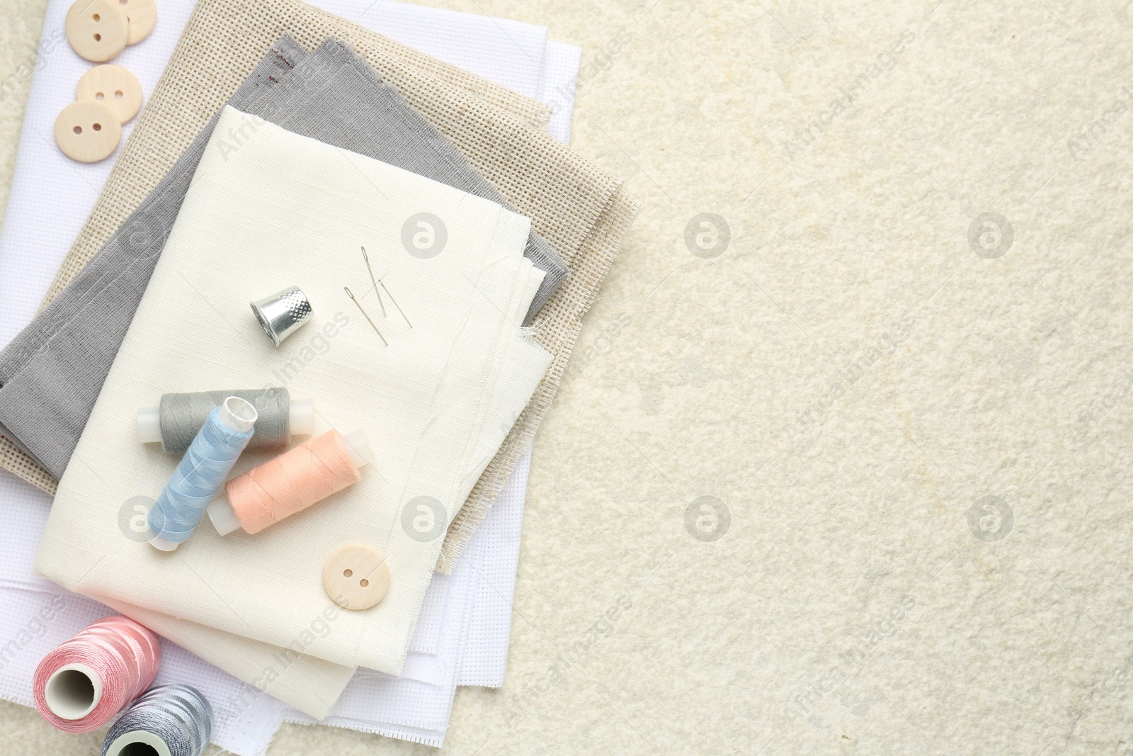 Photo of Different sewing supplies on light textured table, top view. Space for text