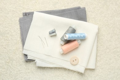 Photo of Different sewing supplies on light textured table, top view