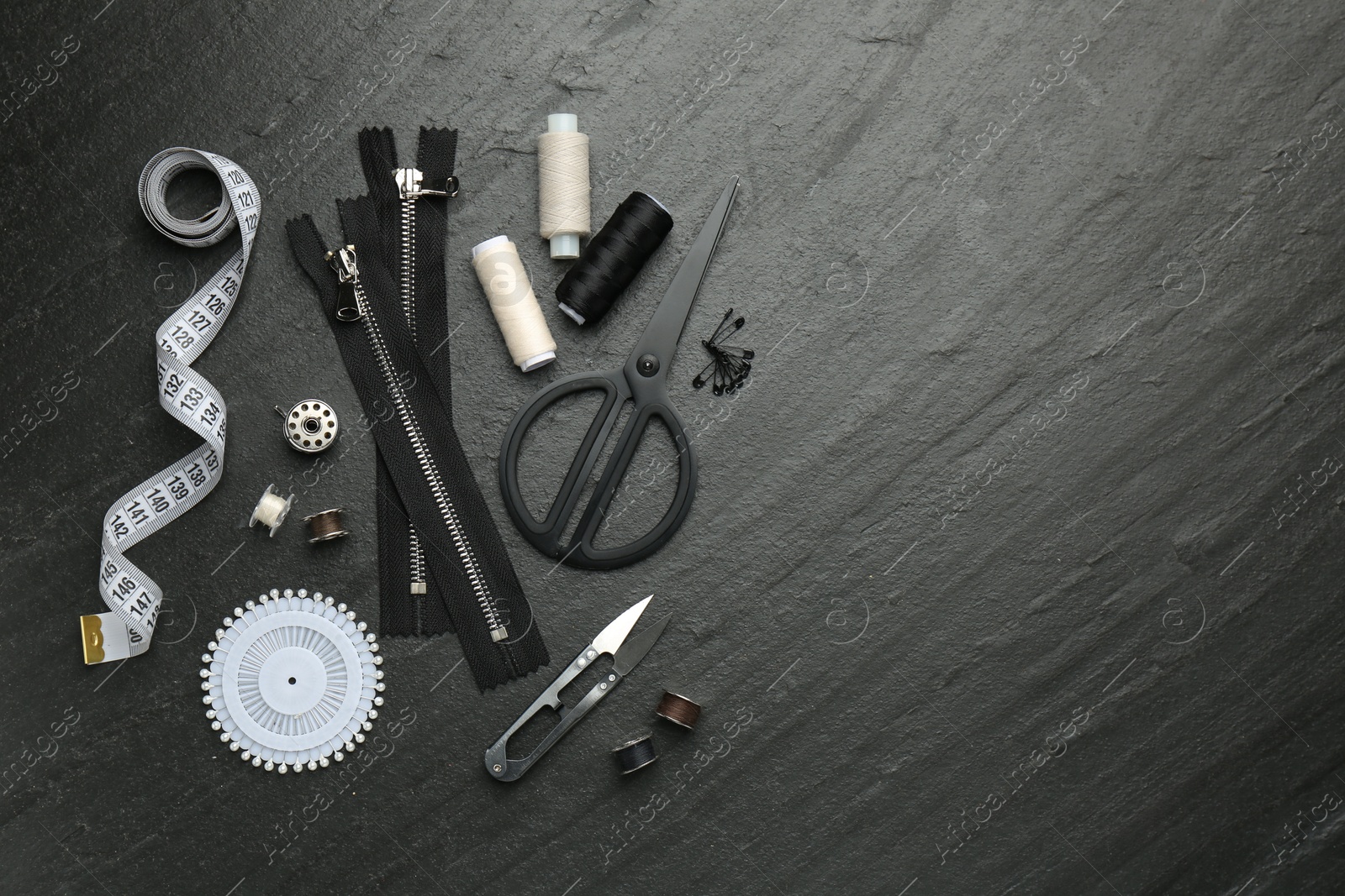 Photo of Flat lay composition with different sewing supplies on dark textured table. Space for text