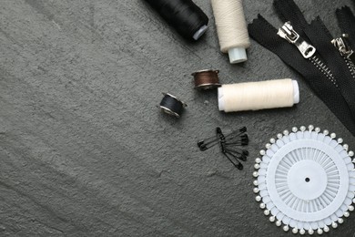 Flat lay composition with different sewing supplies on dark textured table. Space for text