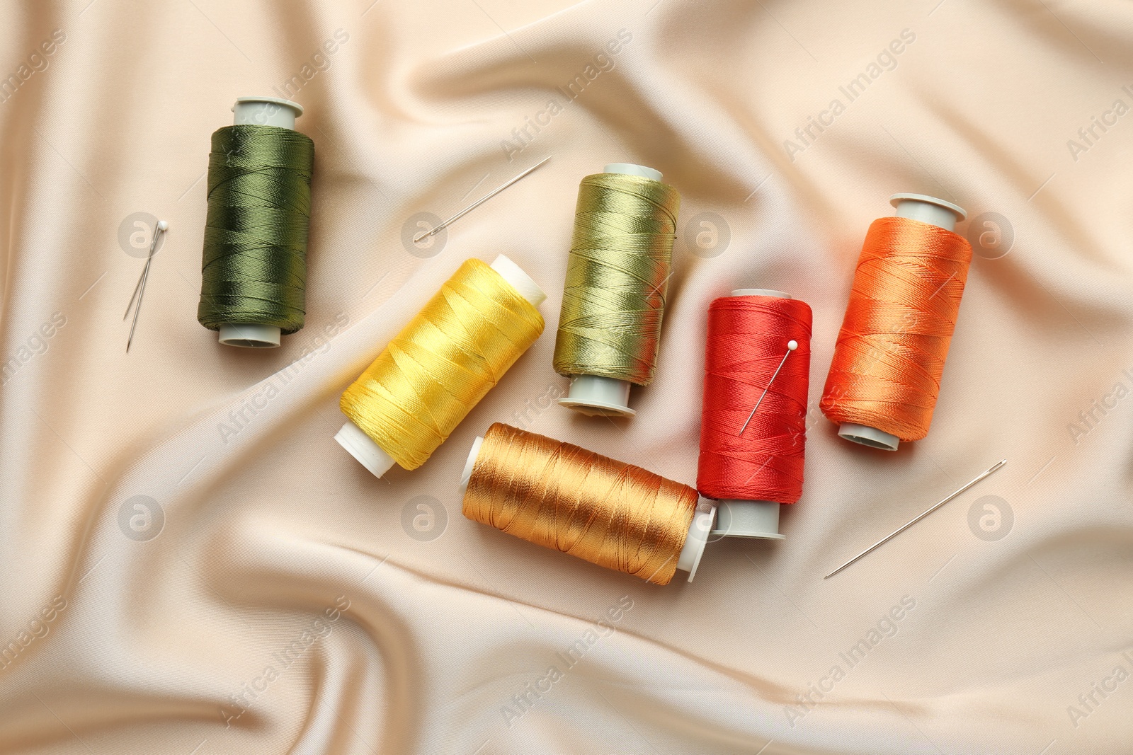 Photo of Spools of sewing threads, pins and needles on beige cloth, top view