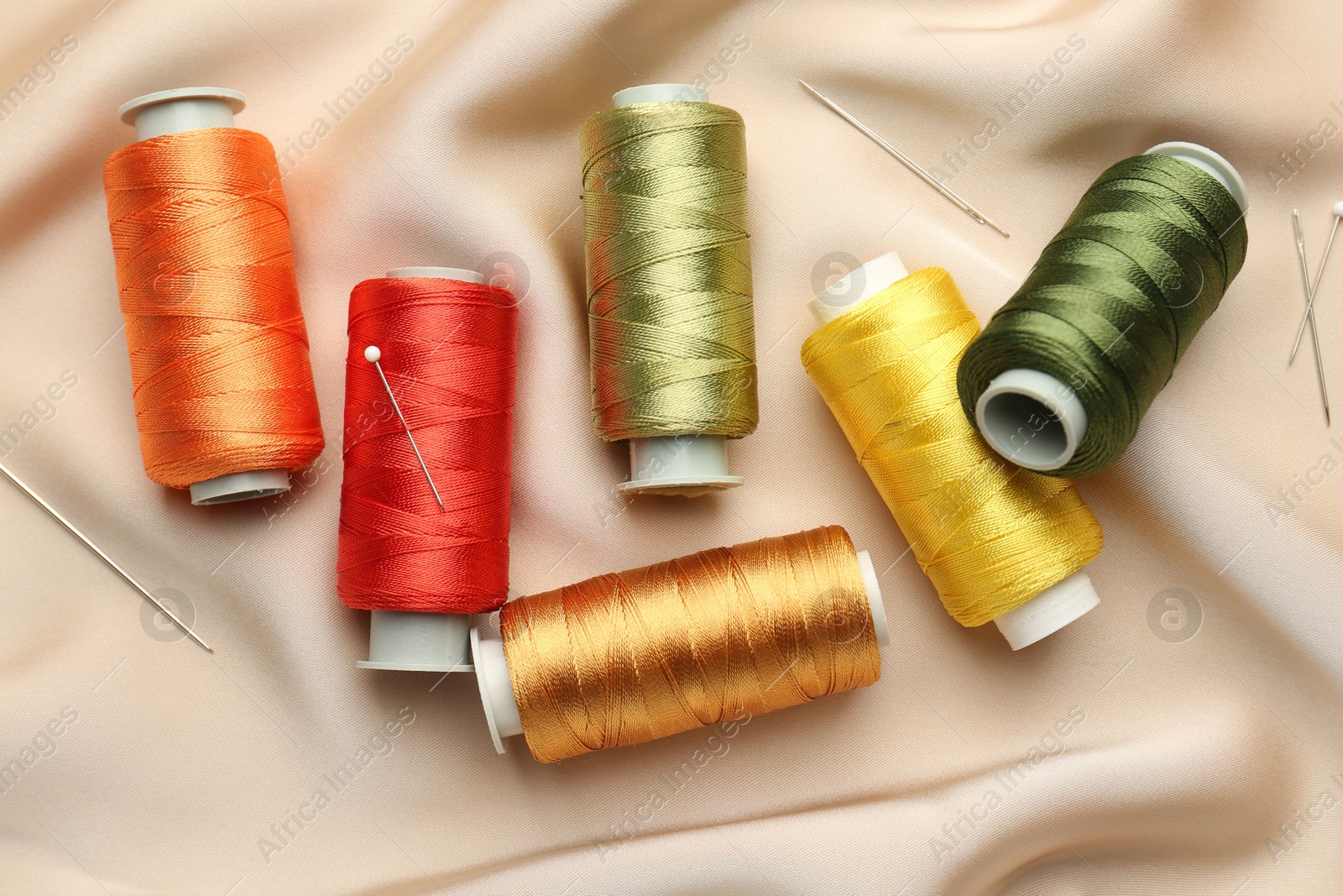 Photo of Spools of sewing threads, pins and needles on beige cloth, top view