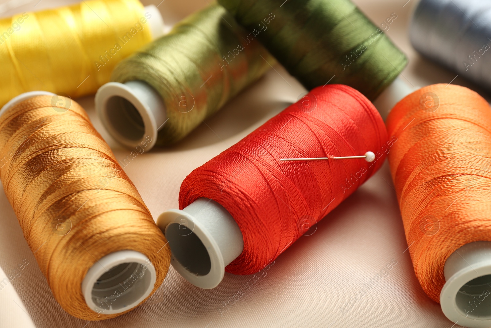 Photo of Spools of sewing threads on beige cloth, closeup