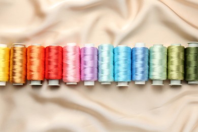 Photo of Spools of sewing threads on beige cloth, top view