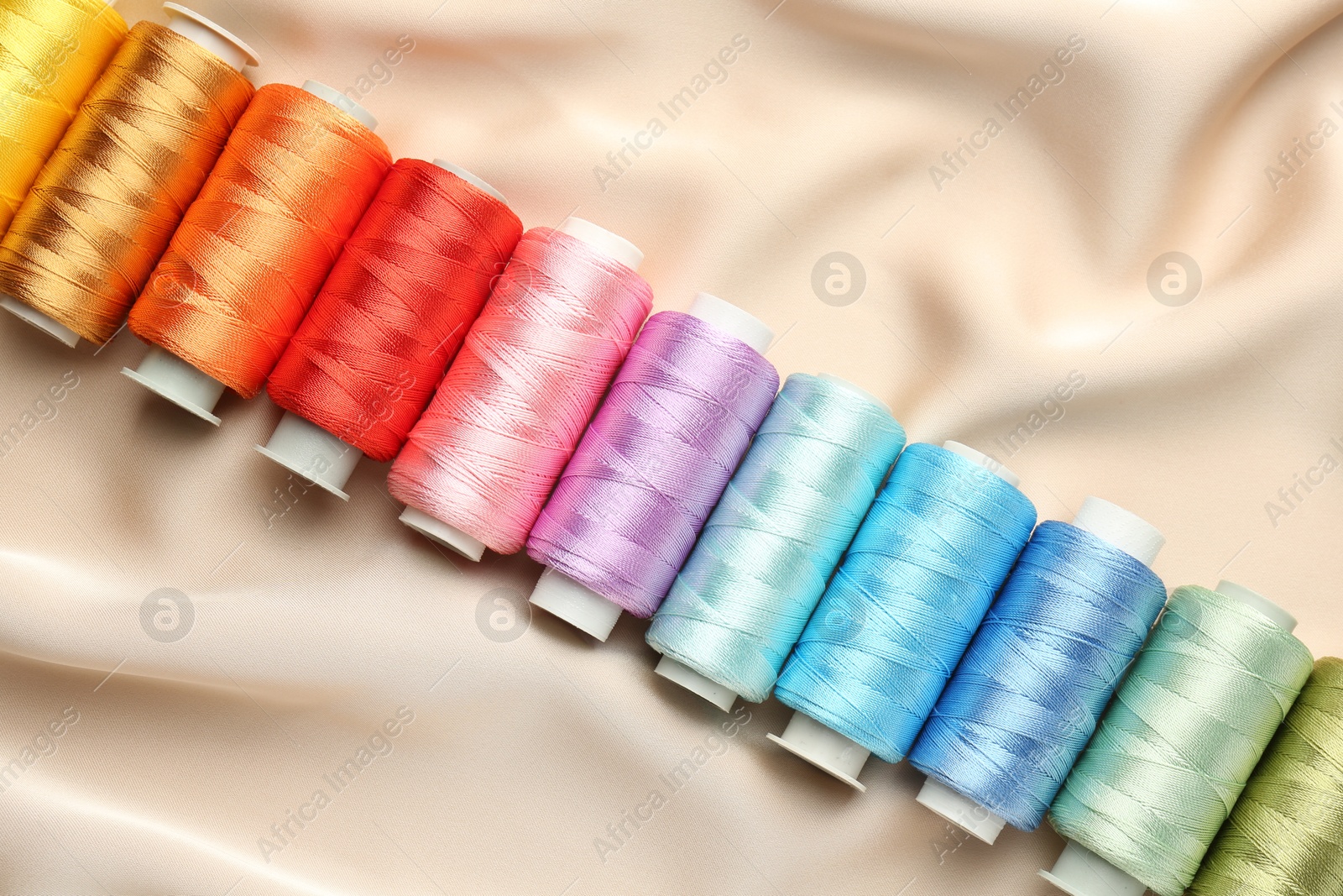 Photo of Spools of sewing threads on beige cloth, top view