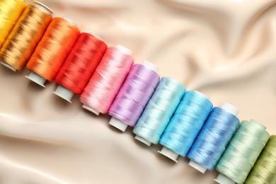 Photo of Spools of sewing threads on beige cloth, top view