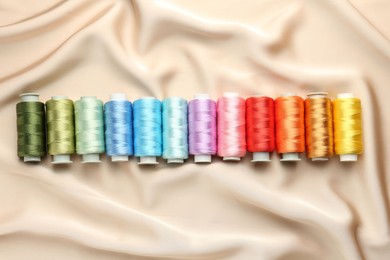 Photo of Spools of sewing threads on beige cloth, top view