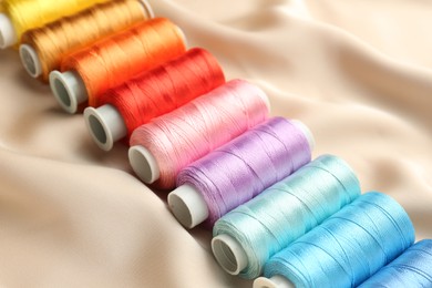 Photo of Spools of sewing threads on beige cloth, closeup