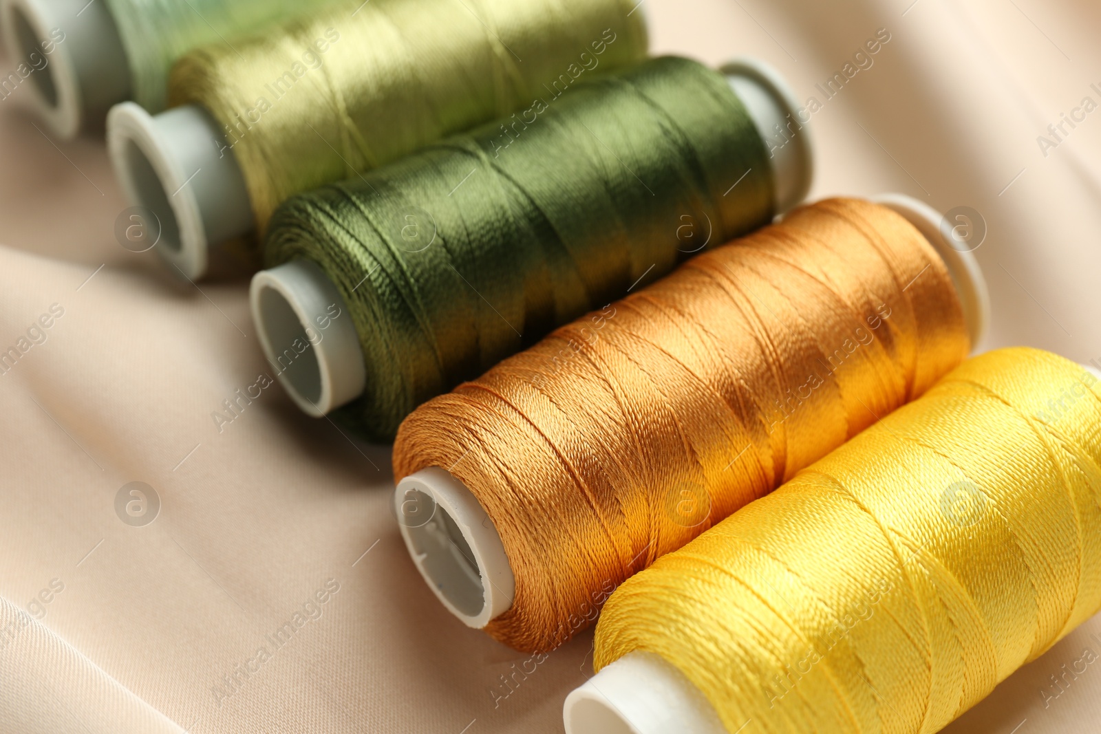 Photo of Spools of sewing threads on beige cloth, closeup