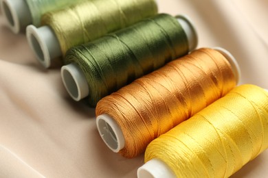 Spools of sewing threads on beige cloth, closeup