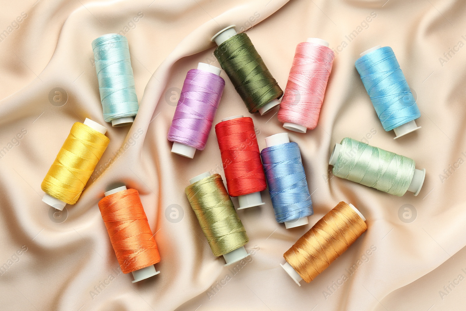 Photo of Spools of sewing threads on beige cloth, top view